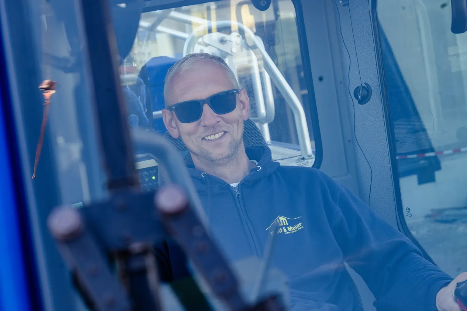 Mitarbeiter mit Sonnenbrille sitzt in einem Fahrzeugcockpit.