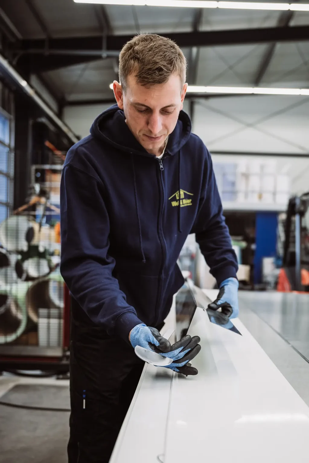 Mitarbeiter bearbeitet Metallbauteil in einer Werkhalle.
