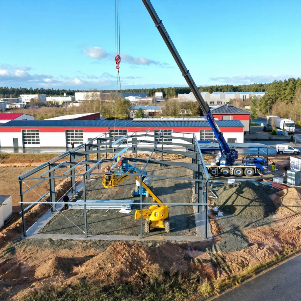 Luftaufnahme einer Baustelle mit Kränen und Hallenbauprojekt.
